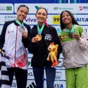 Foto mostra atleta Emanueli Maiara Hein, ao centro, com outras duas atletas. Elas mostram suas medalhas. Ela está com um abrigo esportivo preto com o dizer Times RS.