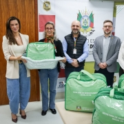 Foto mostra secretários e coordenadoras com kits. Os kits são bolsas verdes. Duas mulheres seguram um dos kits que está dentro de uma banheira branca de bebê.